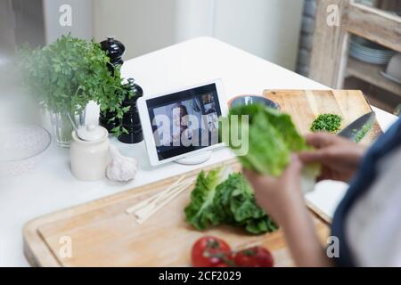 Donna che cucina e video chat con gli amici su tablet digitale schermo Foto Stock