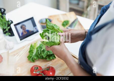 Donna che cucina e video chat con tablet digitale in cucina Foto Stock