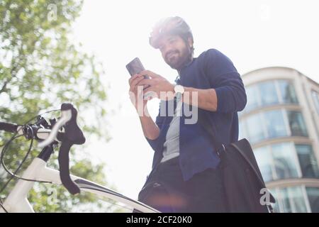 Uomo che usa lo smartphone in bicicletta sotto l'edificio soleggiato Foto Stock