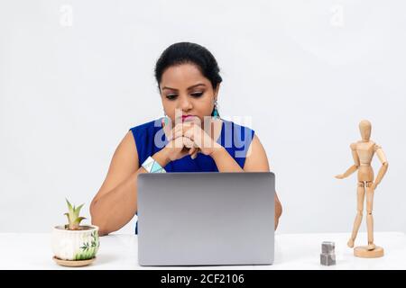 Stanca donna indiana al tavolo, freelancer, lavoro a distanza, lavoro a casa, formazione online, Ufficio di lavoro a casa, perso nei pensieri, mani sul mento. Foto Stock