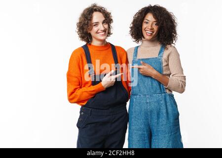 Ritratto di due donne felici in tute che abbracciano e puntano dita l'una sull'altra isolate su sfondo bianco Foto Stock