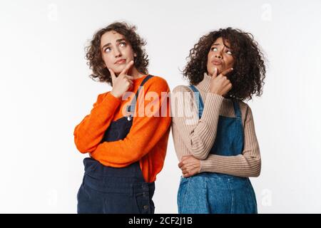 Ritratto di donne multinazionali perplessi in tute pensare e guardare isolato verso l'alto su sfondo bianco Foto Stock