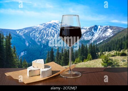 Bicchiere di vino rosso con formaggio brie contro il paesaggio montano. Valle e picchi di montagna in Carpazi durante la soleggiata giornata estiva, Ucraina Foto Stock