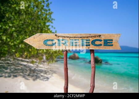 Cartello stradale freccia di legno con parola Grecia contro sfondo spiaggia. Viaggio in Grecia concetto. Foto Stock