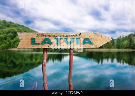 Lettonia freccia di legno cartello stradale contro il lago e sfondo della foresta. Viaggio in Lettonia Concept. Foto Stock