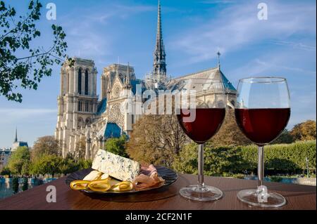 Due bicchieri di vino rosso con assortimento di formaggi e carne contro Notre Dame de Paris o la Cattedrale di Notre-Dame a Parigi, Francia. Festa romantica. Foto Stock