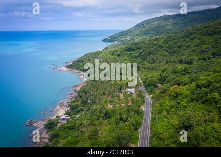 Vista aerea della strada tra palme da cocco e il grande oceano di giorno a Nakhon si Thammarat, Thailandia Foto Stock