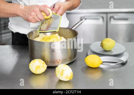 Una mano dello chef Pasticceria grattuce il limone in cucina commerciale.  Lo chef grates si lime sulla grattugia per ottenere la scorza per cucinare,  la preparazione di pasticceria, cibo sano Foto stock 