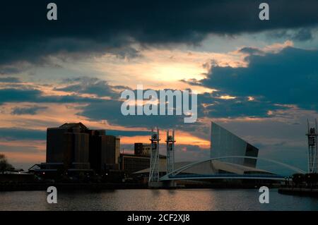 Tramonto sull'edificio Quay West, l'Imperial War Museum North e il ponte pedonale Millennium (Lowry), Salford Quays, Manchester UK. Foto Stock