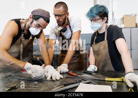 Gruppo di fabbri che fanno coltelli mentre si è in piedi al banco di lavoro in metallo nel vecchio garage Foto Stock