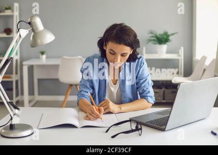 Studente giovane donna che prende appunti durante la lezione online Foto Stock