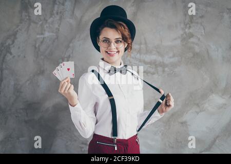 Ritratto di lei bella attraente grazioso soddisfare allegro cheery ragazza con capelli ondulati che tiene nelle mani carte asso che tira suspender isolato su Foto Stock