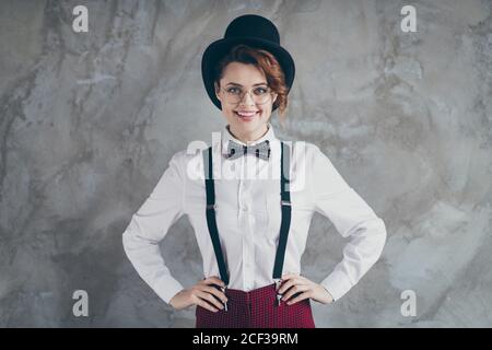 Ritratto di lei bella attraente grazioso soddisfare classy allegra allegria ragazza con capelli ondulati mani su fianchi isolati su grigio calcestruzzo industriale Foto Stock