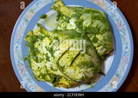 Pomfrets rivestito in una pasta verde fatta di foglie di corriandolo tritato, erbe e spezie viene fritto poco in una padella. Foto Stock