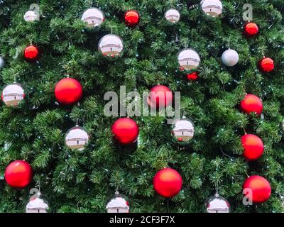 Rami di abete verde con sfere a specchio rosso opaco e argento e piccole luci blu da una ghirlanda Foto Stock