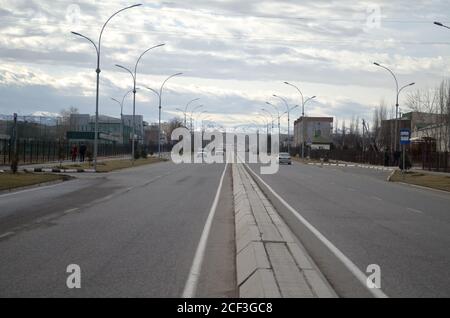 Autostrada in città che si allontana sullo sfondo di montagne e cielo sovrastato, sulla strada andare auto Foto Stock