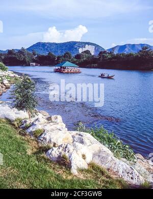 Thailandia, Kanchanaburi. I ristoranti turistici in barca scivolano accanto al famoso Ponte sul Fiume Kwai vicino a quella che era la ferrovia della morte Birmania-Siam della seconda guerra mondiale costruita più o meno dai prigionieri di guerra alleati e la stampa ha ganato la gente locale incaricata di costruire la rotta ferroviaria terrestre da Bangkok nel Golfo di Thailandia a Rangoon in Birmania come parte del piano strategico dell'esercito giapponese imperiale per invadere l'India. Foto Stock