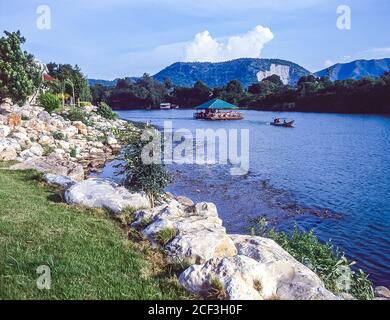 Thailandia, Kanchanaburi. I ristoranti turistici in barca scivolano accanto al famoso Ponte sul Fiume Kwai vicino a quella che era la ferrovia della morte Birmania-Siam della seconda guerra mondiale costruita più o meno dai prigionieri di guerra alleati e la stampa ha ganato la gente locale incaricata di costruire la rotta ferroviaria terrestre da Bangkok nel Golfo di Thailandia a Rangoon in Birmania come parte del piano strategico dell'esercito giapponese imperiale per invadere l'India. Foto Stock