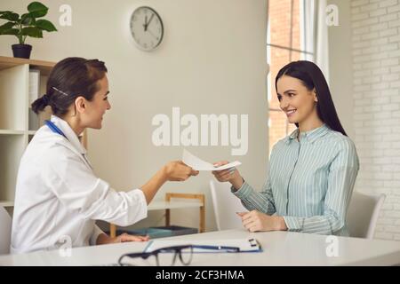 Giovane medico sorridente che dà prescrizione di carta alla paziente di donna dentro clinica medica Foto Stock