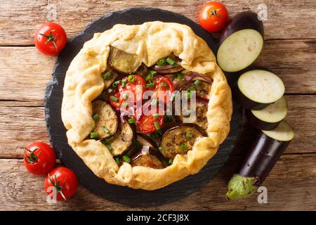 Torta di galette di melanzane piccanti appena sfornata con pomodori, cipolle ed erbe da vicino su un pannello di ardesia sul tavolo. Vista dall'alto orizzontale Foto Stock