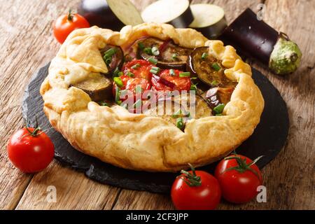 Torta di galette di melanzane piccanti appena sfornata con pomodori, cipolle ed erbe da vicino su una tavola di ardesia sul tavolo. Orizzontale Foto Stock