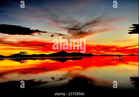 Bellissimo tramonto rosso sulle saline a Salar de Uyuni, Bolivia. Scenografia drammatica del cielo del tramonto. Riflessione nell'acqua del lago. Silhouette scure delle persone. Foto Stock