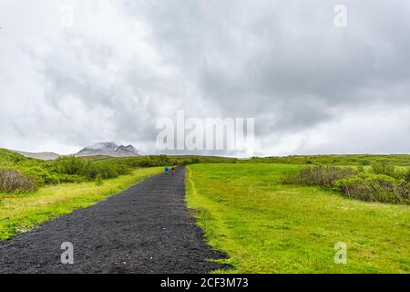 Skaftafell, Islanda verde estate paesaggio e le persone a piedi escursioni su ripido sentiero percorso escursionistico su strada e nuvoloso cielo tempestoso Foto Stock