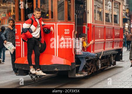 23.10.2019 Istanbul, Turchia. Il tram rosso d'epoca corre lungo la strada di Istanbul, dietro il tram, corre un ragazzo stivato. Primo piano. Il concetto di viaggio Foto Stock