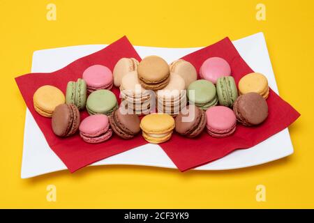 Closeup di colorati macaron francesi sono belli disposti su un piatto bianco su uno sfondo giallo. Dolci, dessert e dolci. Foto Stock