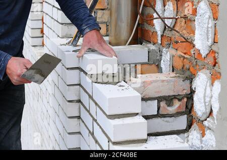 Un closeup di un lavoratore muratore che installa blocchi bianchi e carulking muratura giunti parete esterna con coltello stucco cazzuola all'aperto. Foto Stock