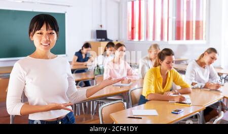 Positiva giovane studentessa asiatica in classe, studentesse che lavorano in background Foto Stock