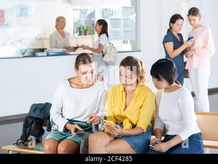 Studenti positivi che si trovano nella sala universitaria e discutono qualcosa di interessante per telefono in pausa Foto Stock
