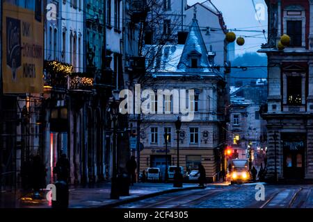 Lviv, Ucraina - 28 dicembre 2019: Piazza del mercato della città vecchia a Lvov con neve invernale nelle notti notturne buie e fari del tram illuminati di colore giallo Foto Stock