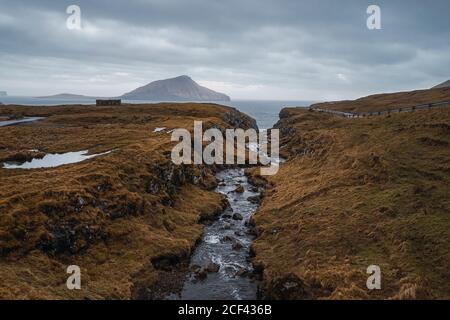 Strada asfaltata curvilinea che attraversa terreni collinosi in giornata nuvolosa Sulle Isole Faroe Foto Stock