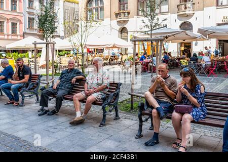 Lviv, Ucraina - 1 agosto 2018: Città vecchia con strada storica sulla piazza del mercato Rynok durante il giorno d'estate le persone sedute sulla panchina mangiare gelato Foto Stock