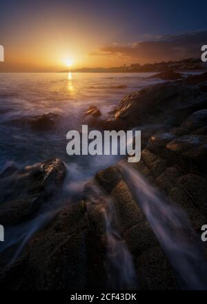 Vista pittoresca di acqua di mare pulita il rotolamento e spruzzi vicino le pietre grezze durante il meraviglioso tramonto Foto Stock