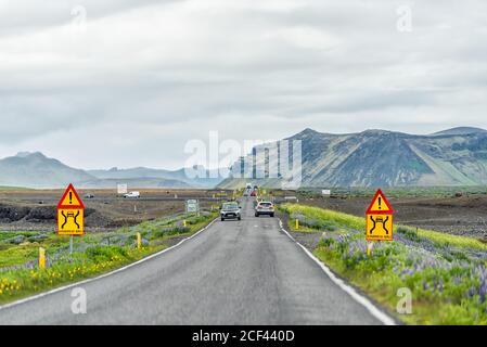 Vik, Islanda - 14 giugno 2018: Cartelli colorati per lo stretto ponte stradale in Islanda con campo di fiori con le auto che passano nel traffico in viaggio su strada circolare Foto Stock