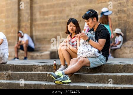 Firenze, Italia - 30 agosto 2018: Coppie di turisti giovani asiatici seduti sulla piazza fuori durante il giorno d'estate a Firenze, Toscana Foto Stock