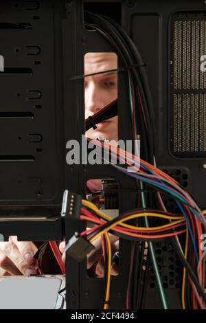 Giovane uomo ripara un'unità di sistema di computer, cambia parti, scheda video e disco rigido, imposta nuovi componenti. Ripristino guidato del computer Foto Stock