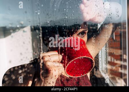 Donna premurosa bere caffè vicino alla finestra Foto Stock