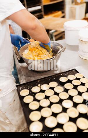 Crop confectioner in guanti e miscelazione uniforme e impastare morbido pasta fresca mentre si prepara la pasticceria in panetteria Foto Stock