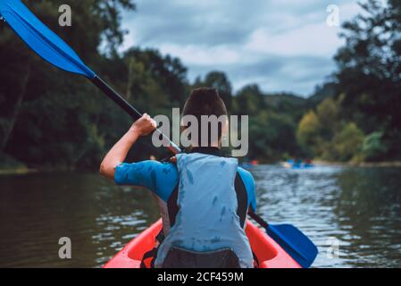 Vista posteriore dello sportivo seduto in canoa rossa e pagaia sul declino del fiume Sella in Spagna Foto Stock