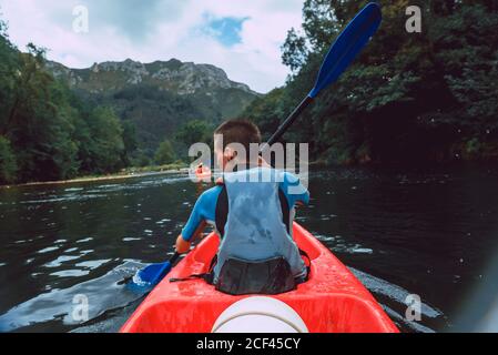 Vista posteriore dello sportivo seduto in canoa rossa e pagaia sul declino del fiume Sella in Spagna Foto Stock