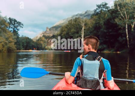 Vista posteriore dello sportivo seduto in canoa rossa e pagaia sul declino del fiume Sella in Spagna Foto Stock