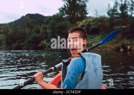 Vista posteriore dello sportivo seduto in canoa rossa e pagaia sul declino del fiume Sella in Spagna Foto Stock