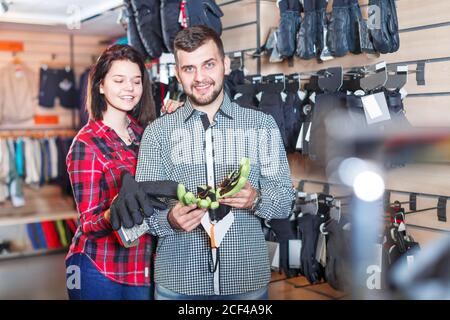 Giovane coppia che sceglie un guanti di protezione in un negozio di abbigliamento sportivo. Focus sull'uomo Foto Stock