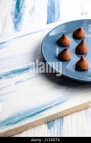 Da sopra piatto blu con cioccolato a forma di cono fatto in casa caramelle su tavola rustica in legno Foto Stock