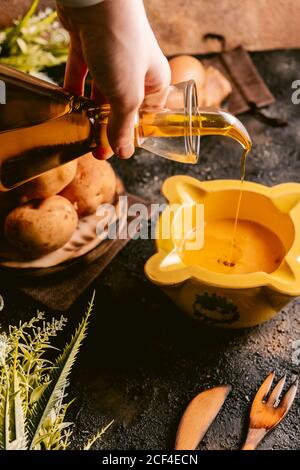 Da sopra di raccolto Donna versando olio in ciotola preparazione per cucinare piatto in cucina Foto Stock