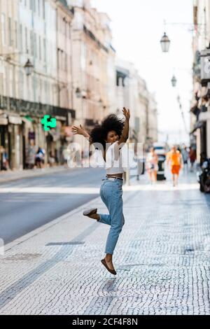 Donna etnica felice in trendy salto vestito per la gioia e guardare la macchina fotografica il giorno d'estate Foto Stock