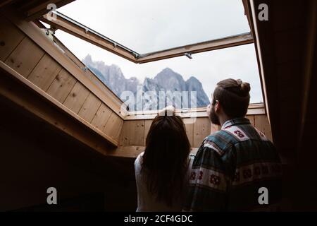 Da sotto la vista posteriore dei viaggiatori maschili e femminili senza volto In abbigliamento informale ammirando il paesaggio delle Dolomiti in Italia dal lucernario Foto Stock